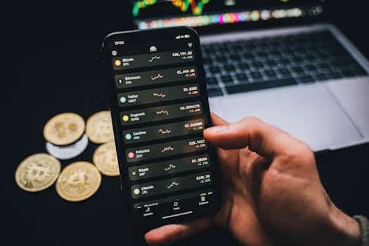 A person checks cryptocurrency values on a smartphone with a laptop and Bitcoins nearby.